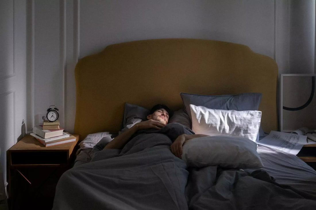 Une personne qui dort sur son lit et il y a un réveil à coté de lui prêt à sonner
